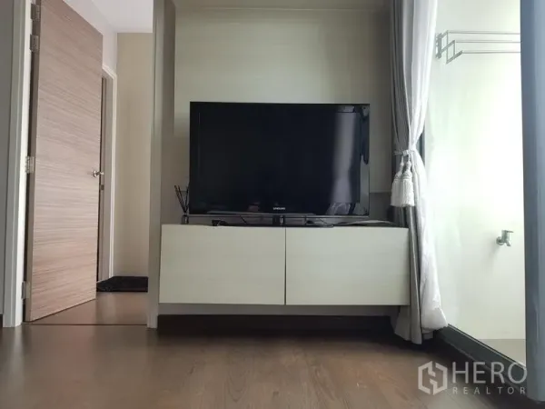 公寓 出租在Ratchathewi, Bangkok - 落地窗旁的悬空电视柜与平板电视，配有窗帘。