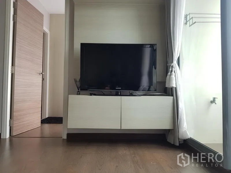 公寓 出租在Ratchathewi, Bangkok - 落地窗旁的悬空电视柜与平板电视，配有窗帘。