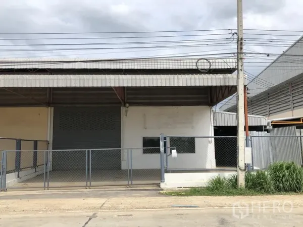 工厂 出租在Lat Lum Kaeo, Pathum Thani - 工厂外观，带遮雨装卸平台、卷闸门和铁丝网围栏大门。