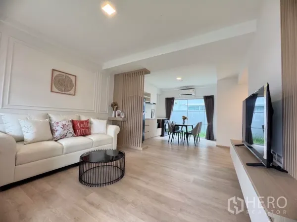 联排别墅 出租在Prawet, Bangkok - 开放式客餐厅，白色沙发、木地板与可见的厨房。