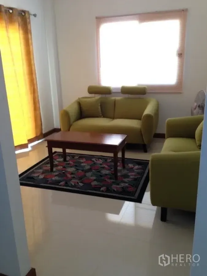 独立式住宅 出售在Phra Khanong, Bangkok - 采光良好的起居区，配两张绿色沙发、茶几与窗帘。