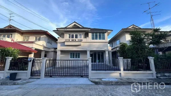 บ้าน ให้เช่าในLat Krabang, Bangkok - ด้านหน้าบ้านเดี่ยวสองชั้นในย่านลาดกระบัง พร้อมรั้วและที่จอดรถ หลังคากระเบื้องท่ามกลางท้องฟ้าสีฟ้า