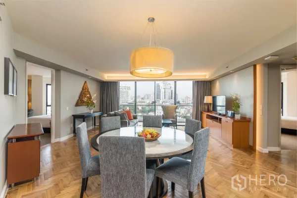 Condominium for rent in Yan Nawa, Bangkok - Bright open-plan living and dining room with a round marble table, pendant light, parquet flooring, TV console and large windows with Bangkok skyline views.