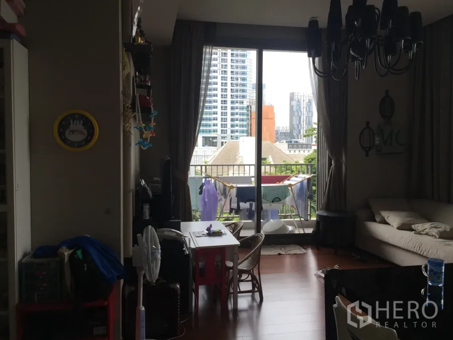 Condominium for sale in Watthana, Bangkok - Open-plan living and dining room with sofa, dining set, and sliding doors to a balcony with city views in Thonglor Bangkok.