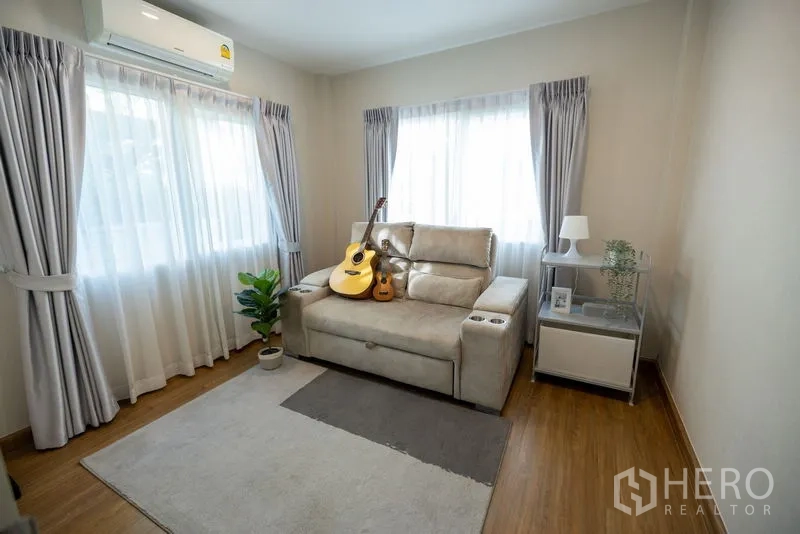 Detached House for rent or sale in Bang Phli, Samut Prakan - Bright sitting room with reclining sofa, guitars, sheer curtains and wood flooring.