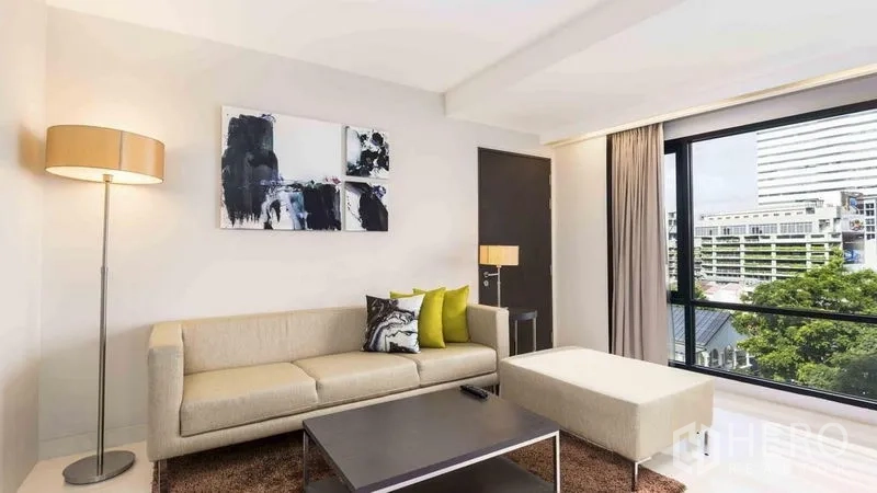 Apartment for rent in Watthana, Bangkok - Cozy sitting area with sofa, ottoman and city-view window.