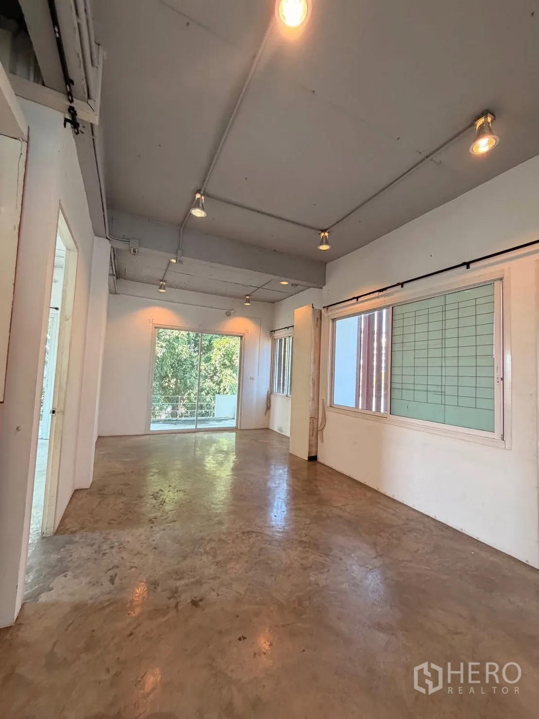 สำนักงานที่บ้าน for rent in Huai Khwang, Bangkok - ห้องโถงเปิดโล่ง พื้นปูนขัดมัน ผนังสีขาว ไฟราง และหน้าต่างบานใหญ่