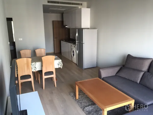 คอนโด ให้เช่าในBangkok - พื้นที่นั่งเล่นและรับประทานอาหารแบบเปิด พร้อมโซฟา โต๊ะกาแฟไม้ และครัวเล็กมีตู้เย็นกับเครื่องซักผ้า