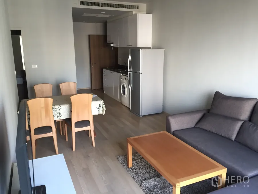 คอนโด ให้เช่าในBangkok - พื้นที่นั่งเล่นและรับประทานอาหารแบบเปิด พร้อมโซฟา โต๊ะกาแฟไม้ และครัวเล็กมีตู้เย็นกับเครื่องซักผ้า