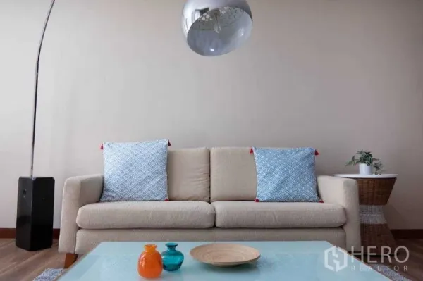 Condominium for rent in Pathum Wan, Bangkok - Warm living room with cream sofa, blue cushions, glass coffee table and arc floor lamp