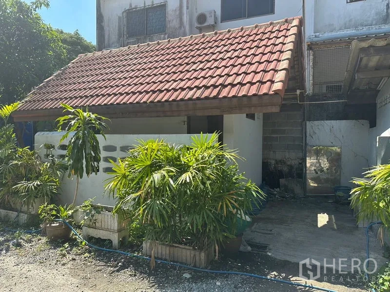 Warehouse for rent in Suan Luang, Bangkok - Small on-site office or guard house with red tiled roof and tropical plants at the entrance.