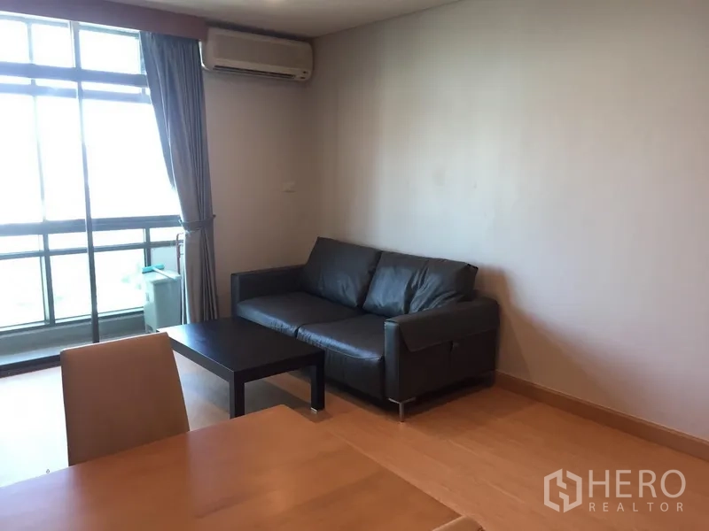 Condominium for rent in Sathon, Bangkok - Living room with black leather sofa, coffee table and floor-to-ceiling windows to balcony.
