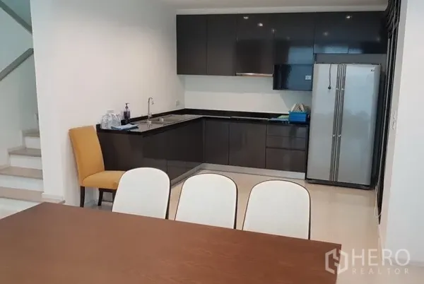 独立式住宅 出租在Prawet, Bangkok - 开放式餐区与L形厨房，亮面深色橱柜、水槽与双开门冰箱。