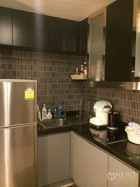 Condominium for rent in Watthana, Bangkok - Compact L-shaped kitchen with dark tile backsplash and black countertops.