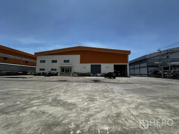 Warehouse for rent - Front view of an orange-roof warehouse with a two-storey office and wide concrete yard.
