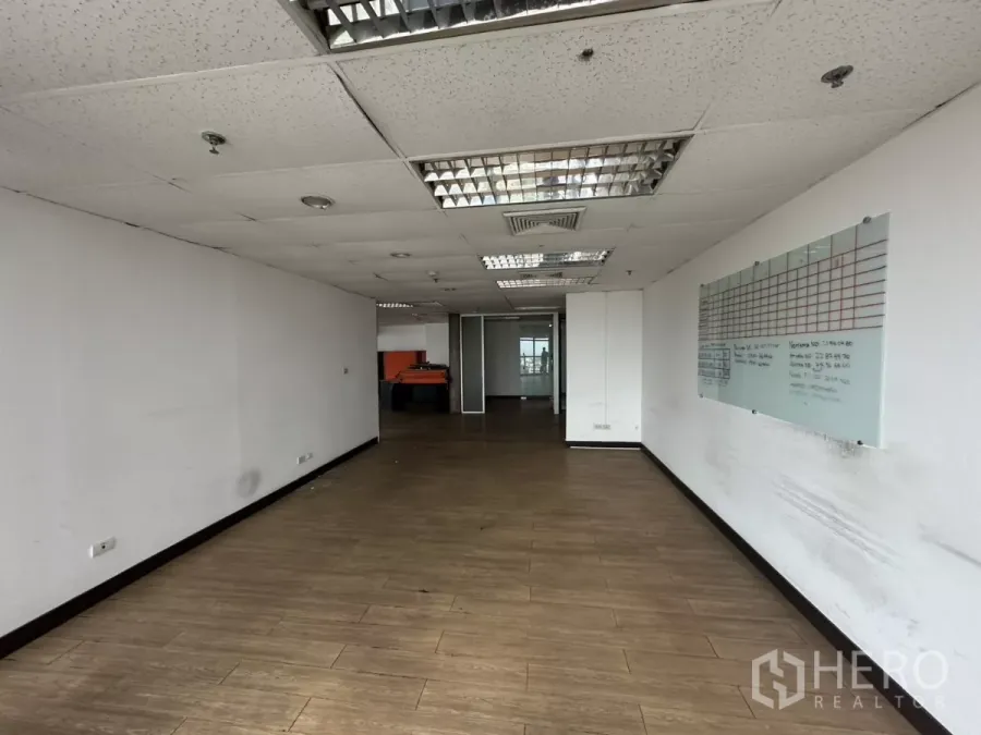 Office Space for rent in Watthana, Bangkok - Enclosed office area with wood-look floors, dropped ceiling with fluorescent lights, and a wall-mounted planning board.