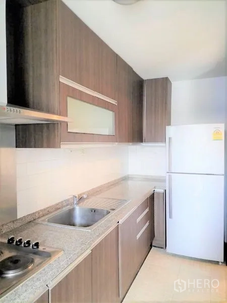Condominium for rent in Watthana, Bangkok - Compact kitchen with wood cabinetry, granite countertops, electric hob, hood, sink and refrigerator.