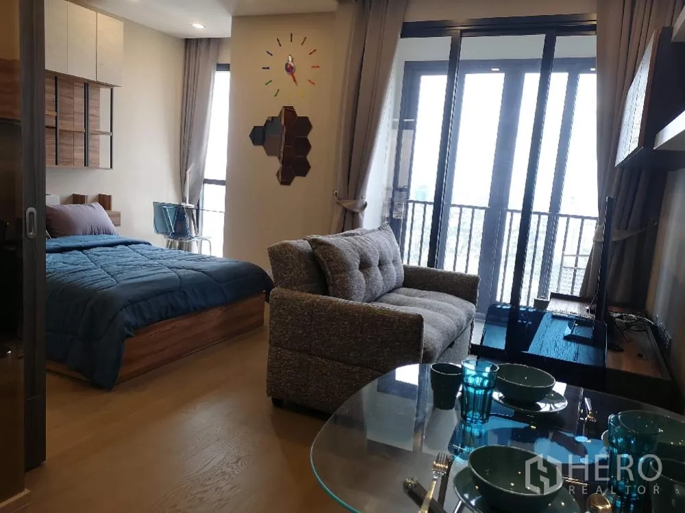 Condominium for rent in Watthana, Bangkok - Bright living and bedroom area with floor-to-ceiling windows opening to a balcony and city view, plus sofa and TV console.