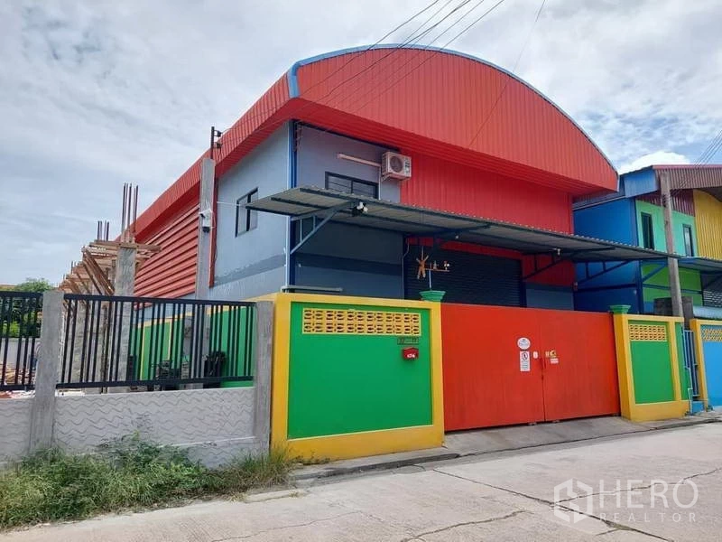 货栈 出租或出售在Bang Bua Thong, Nonthaburi - 仓库立面侧视图，带雨棚装卸区与坚固红色大门。