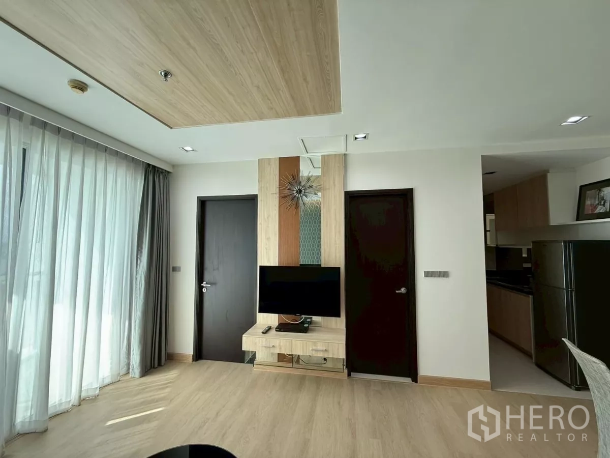 คอนโด ให้เช่าในWatthana, Bangkok - พื้นที่นั่งเล่นมีชั้นวางทีวี หน้าต่างสูงระดับระเบียง และประตูไม้สีเข้มสองบาน