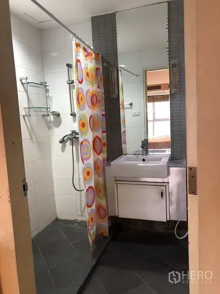 Condominium for rent in Khlong Toei, Bangkok - Compact bathroom with shower, colorful curtain, vanity and mirror.