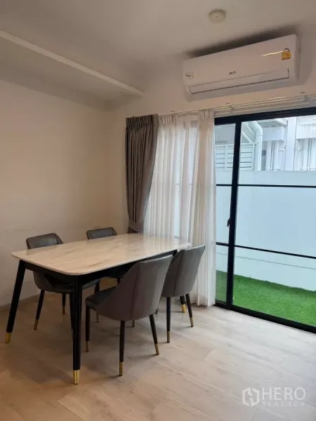 Townhouse for rent in Bang Phli, Samut Prakan - Dining space with air conditioner and sliding glass door to a small grassed yard.