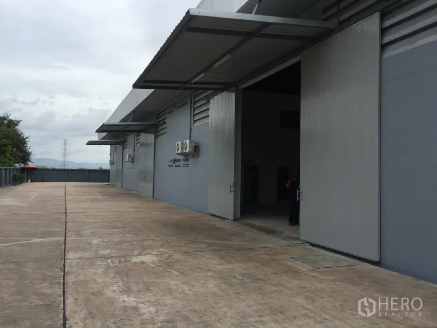 工厂 出租在Si Racha, Chon Buri - 厂房外部装卸区，宽大推拉金属门、雨棚与宽阔混凝土车道。