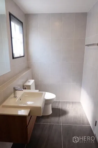 Detached House for rent in Bang Phli, Samut Prakan - Contemporary tiled bathroom with vanity, mirror, toilet and a window for natural light.