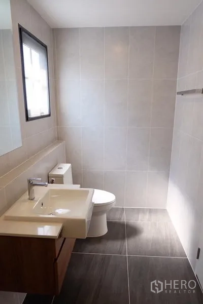 Detached House for rent in Bang Phli, Samut Prakan - Contemporary tiled bathroom with vanity, mirror, toilet and a window for natural light.