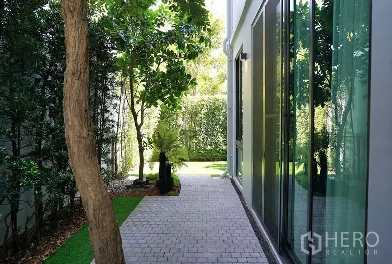 Detached House for rent in Saphan Sung, Bangkok - Shaded side garden walkway with mature trees and full-height glass windows.