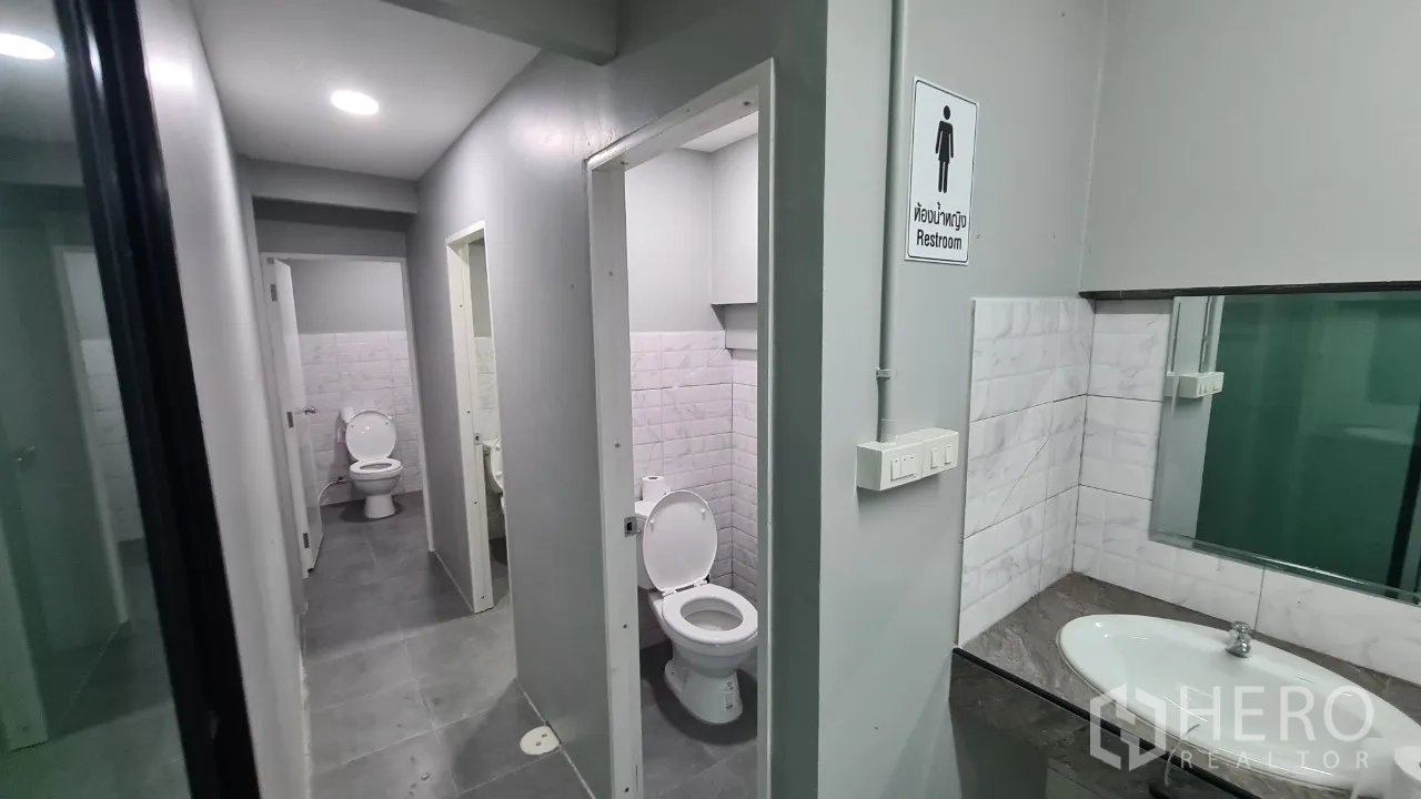 Home Office for rent in Pathum Thani - Clean restroom zone with multiple toilet stalls, grey floor tiles and a countertop sink.