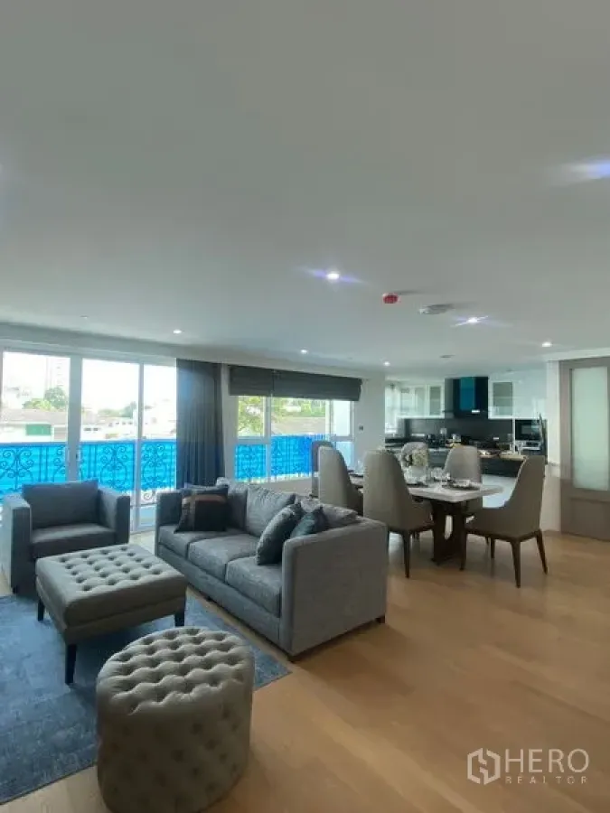Condominium for rent in Watthana, Bangkok - Open-plan living and dining area with balcony featuring blue railing and a modern kitchen at the back.