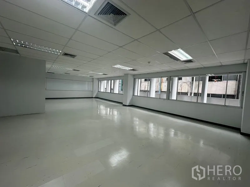 Office Space for rent in Bang Rak, Bangkok - Open-plan office with white vinyl floors, drop ceiling, and a long row of windows providing natural light.
