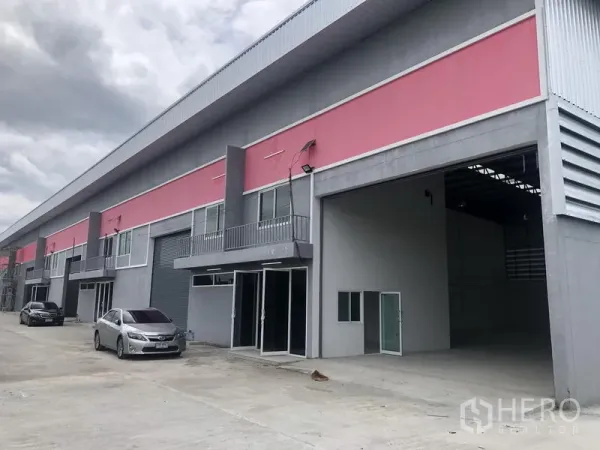 工厂 出租在Sai Noi, Nonthaburi - 成排工厂仓库单元，开放式装卸区，车辆停放在宽阔混凝土车道上。