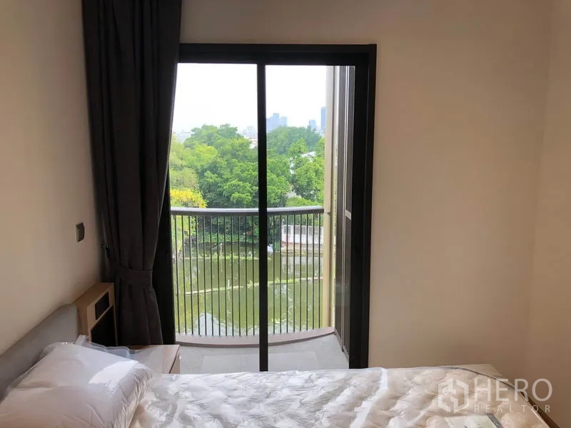 คอนโด ให้เช่าในWatthana, Bangkok - ห้องนอนที่สองมีเตียงเดี่ยวและประตูกระจกสไลด์ออกระเบียง เห็นวิวคลองและต้นไม้