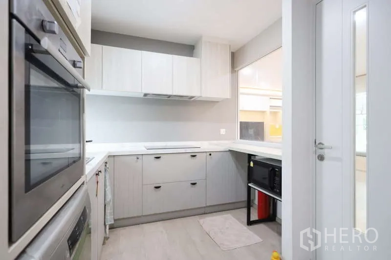 Detached House for rent or sale in Prawet, Bangkok - Light-toned L-shaped kitchen with built-in appliances, ample cabinets and a window.