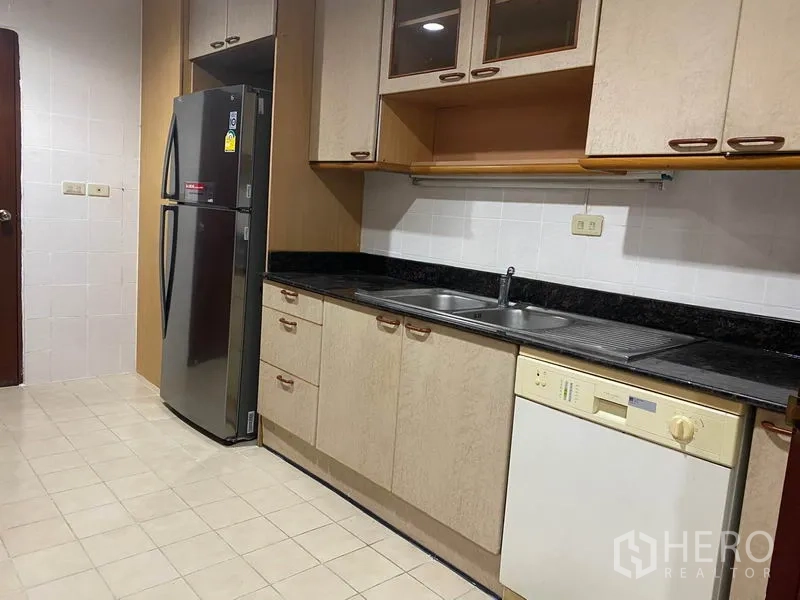 Condominium for rent in Watthana, Bangkok - Kitchen opposite side showing double sink, dishwasher, black granite counters and tall fridge.