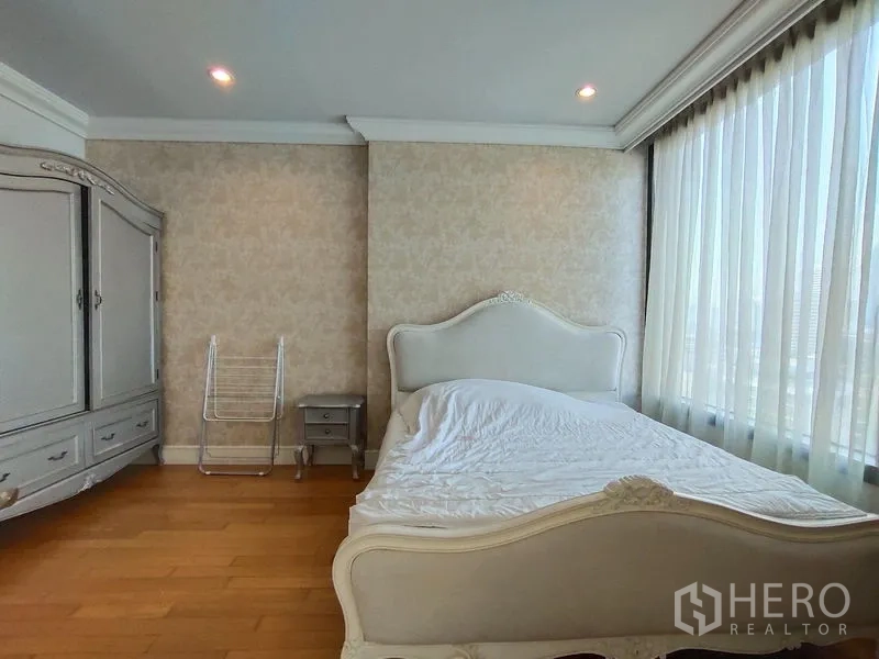 公寓 出租在Khlong Toei, Bangkok - 转角卧室，落地窗与木地板，经典白色床与衣柜，远眺城市天际线