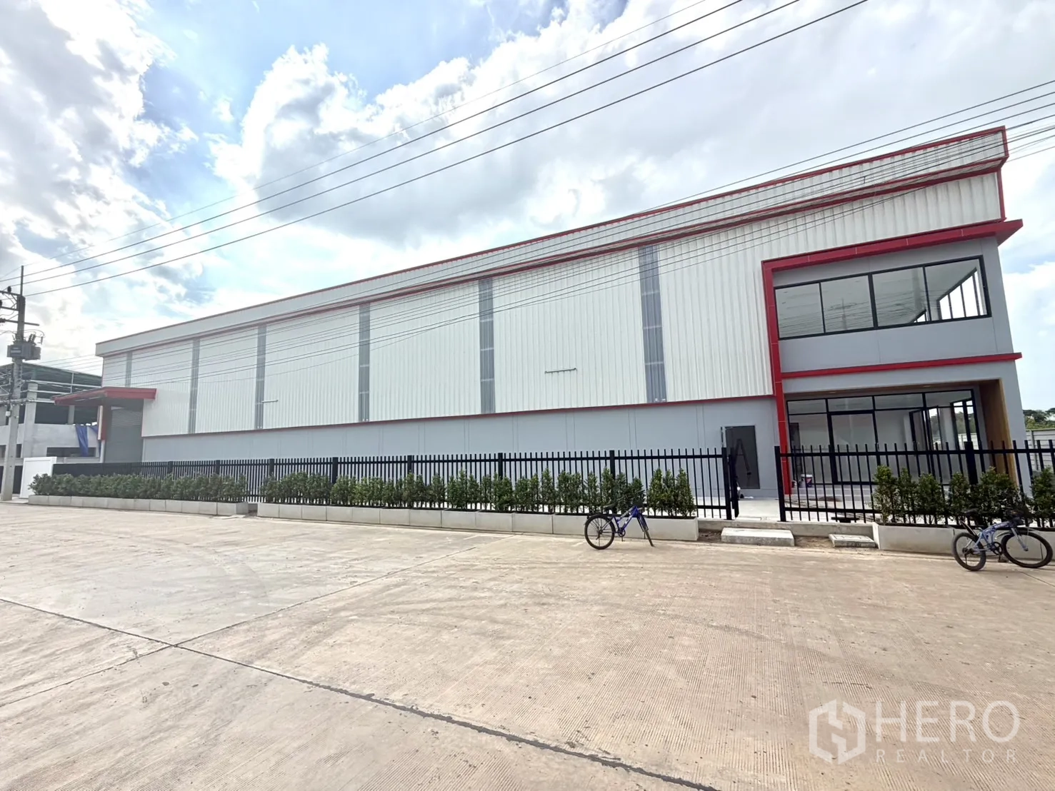 Factory for rent or sale in Lam Luk Ka, Pathum Thani - Factory exterior with a corner glass-fronted office wing and planted frontage.