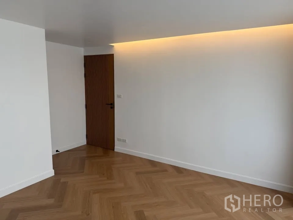 Condominium for rent in Watthana, Bangkok - Empty room with herringbone wood floor and cove lighting.