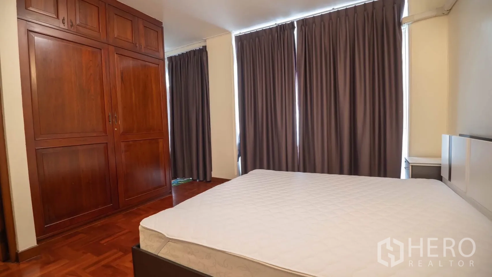Townhouse for rent in Watthana, Bangkok - Bedroom with built-in wooden wardrobes and large windows with dark curtains.