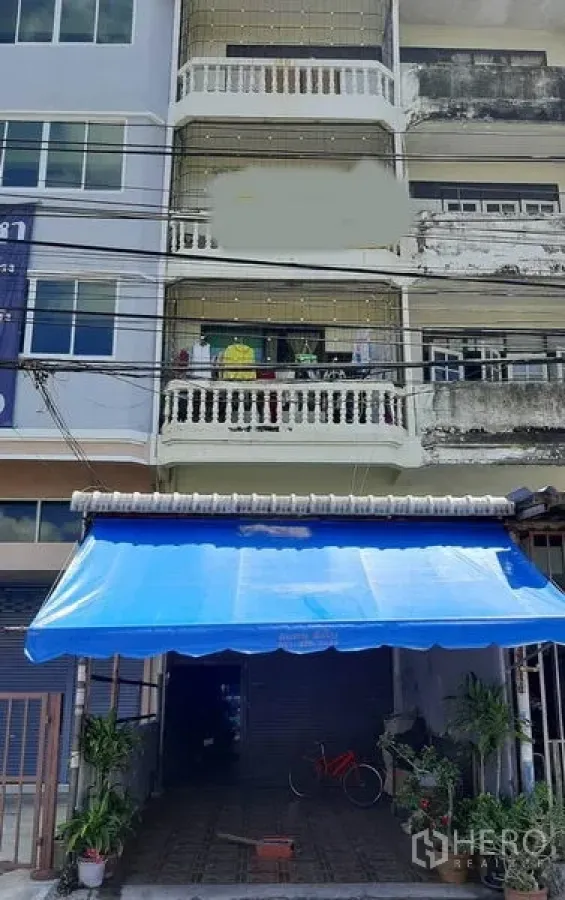 零售空间 出售在Bang Na, Bangkok - 曼谷邦纳四层临街商铺外立面，蓝色遮阳棚、卷闸门与阳台及门前绿植