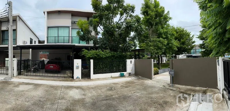 独立式住宅 出售在Samut Prakan - 街景视角，带围墙与大门的住宅入口，绿树成荫。