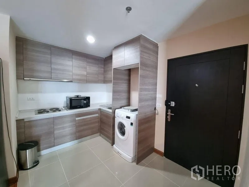 Condominium for rent in Huai Khwang, Bangkok - Compact L-shaped kitchen with cooktop, microwave and washing machine.