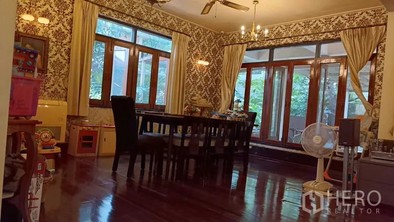 独立式住宅 出租在Phaya Thai, Bangkok - 餐厅配实木地板、吊灯与复古墙纸，宽幅窗户通向花园景观。