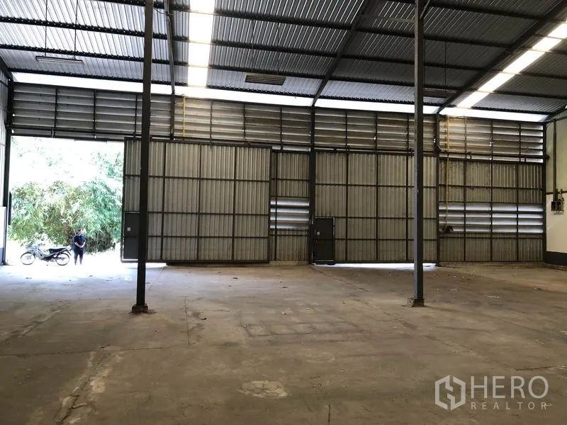 Warehouse for rent in Lam Luk Ka, Pathum Thani - Wide sliding metal doors and loading access inside a high-clearance warehouse with ventilation louvers.