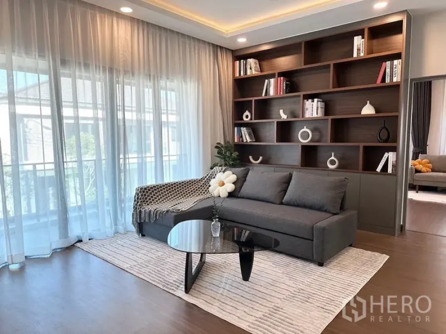Detached House for rent or sale in Bang Phli, Samut Prakan - Bright upstairs lounge with sofa, built‑in wood bookshelf and sheer curtains.