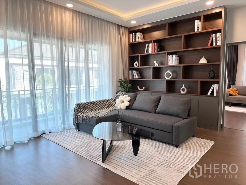 Detached House for rent or sale in Bang Phli, Samut Prakan - Bright upstairs lounge with sofa, built‑in wood bookshelf and sheer curtains.