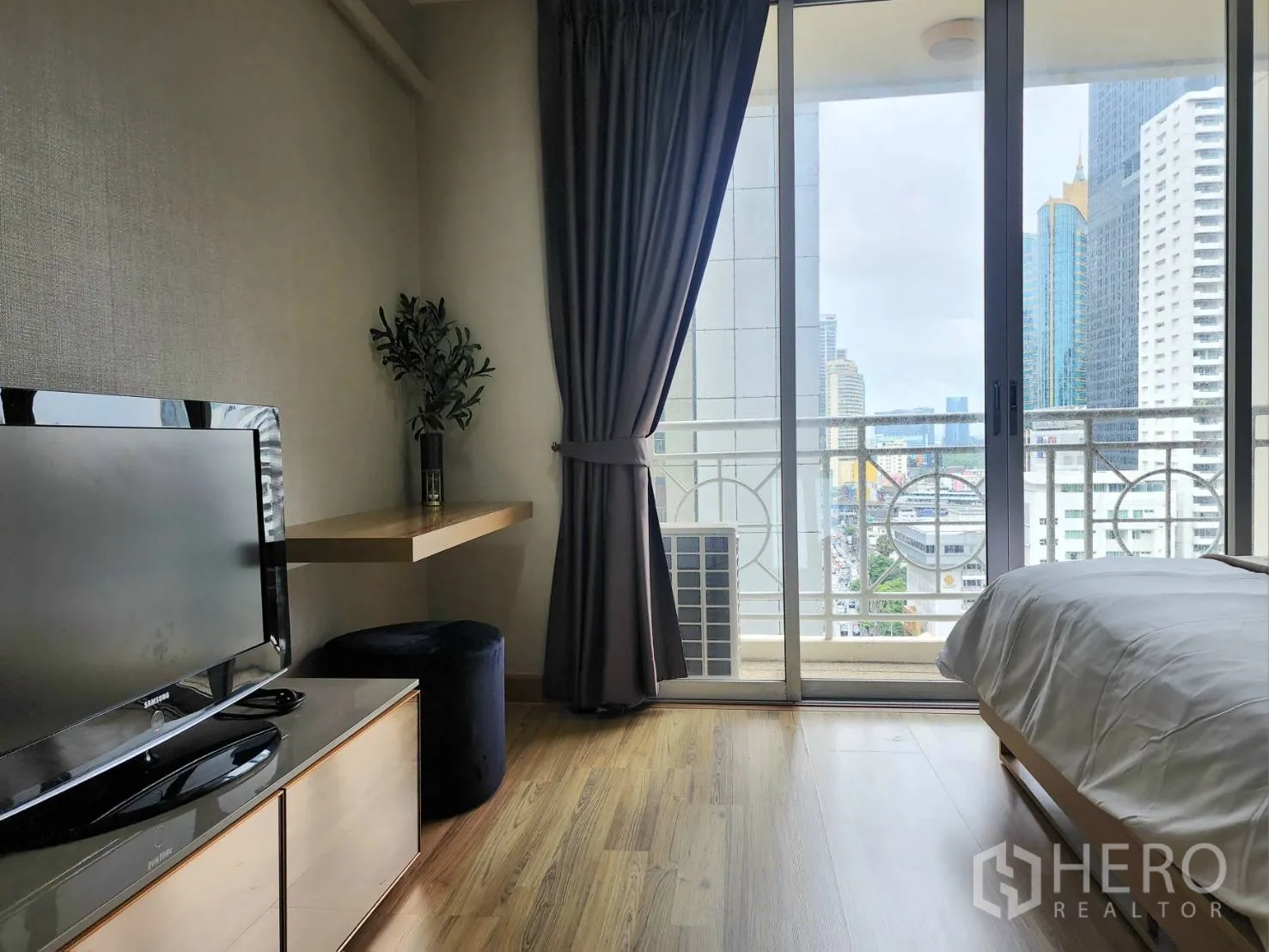 Condominium for rent in Watthana, Bangkok - Bedroom corner with TV, wall-mounted desk and sliding doors to a balcony and city view.