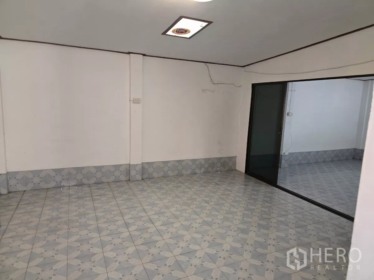 Home Office for rent in Wang Thonglang, Bangkok - Empty multipurpose room with patterned floor tiles, white walls and a sliding glass partition.
